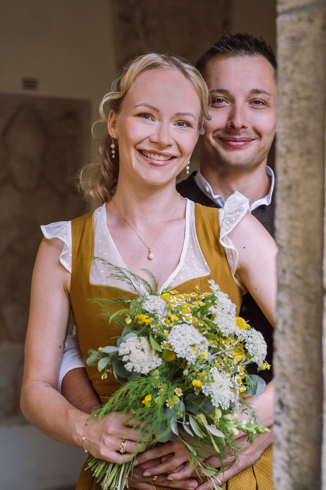 Brautpaar in Tracht mit Wiesenblumenstrauß – Brautstyling Bronze
