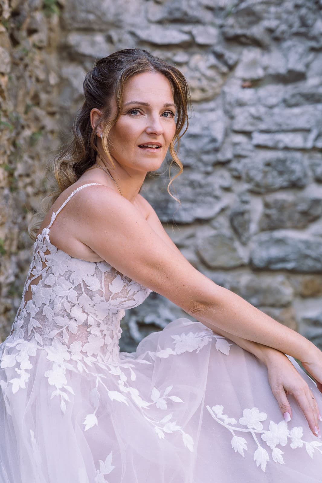 Braut mit halboffener Frisur vor Steinmauer – Brautstyling Silber